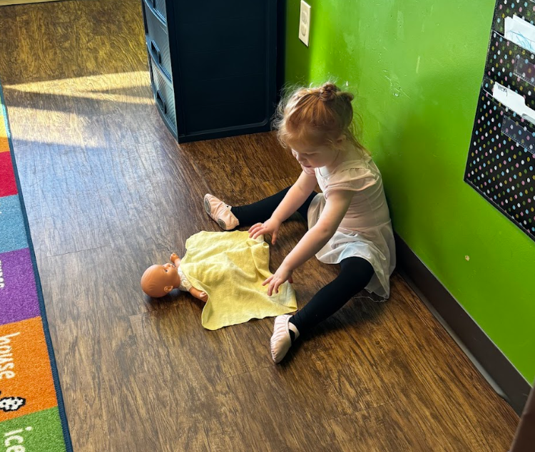 Toddler at Tiny People Childcare Center in Magnolia, TX caring for a baby doll, a behavior that has been modeled for her. 